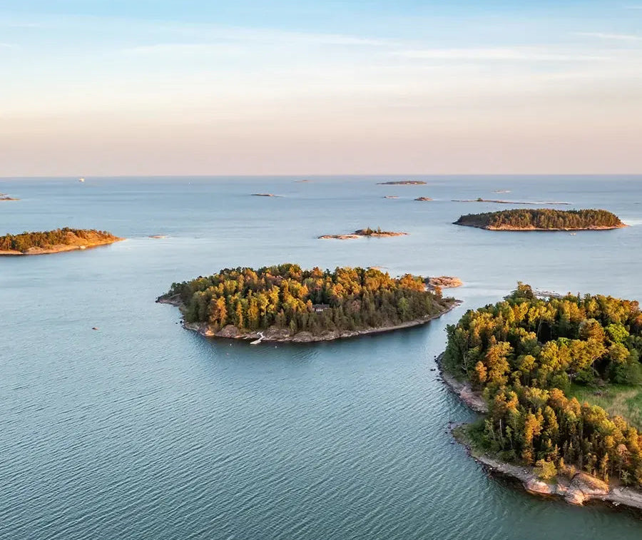 Aerial view of a calm blue sea with several small forested islands under a pale sky.